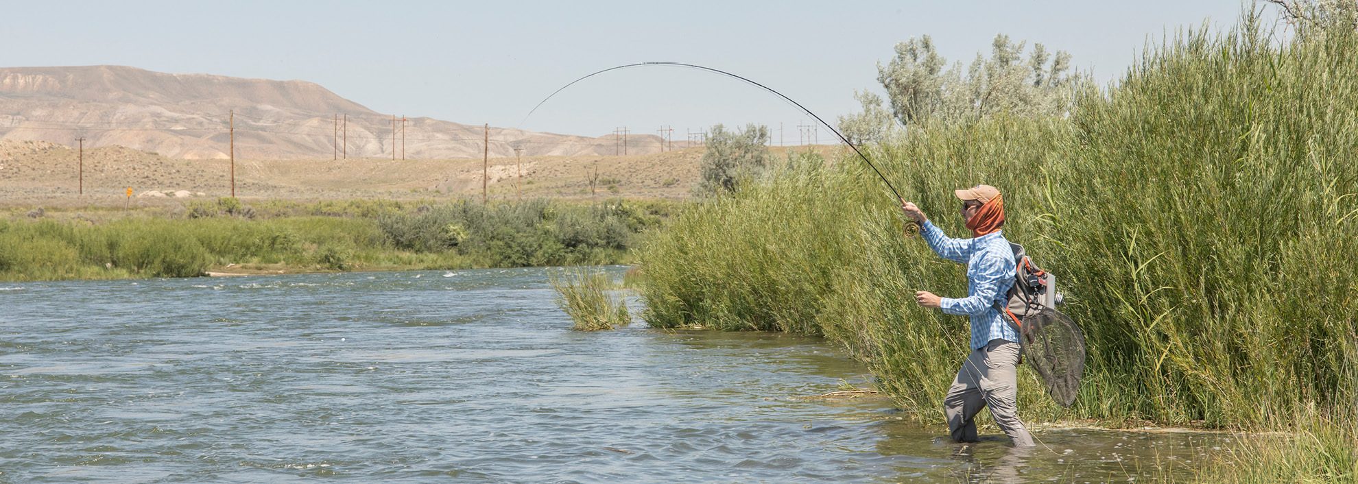 Man fly fishing in river with mountain in the background